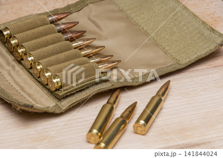 Rifle cartridges arranged in tan ammunition pouch with extra rounds nearby 141844024