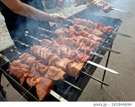 High angle shot of succulent pork shashlik kebabs grilling on metal skewers over hot coals for outdoor picnic barbecue lunch preparation High angle shot of succulent pork shashlik kebabs grilling on metal skewers over hot coals for outdoor picnic barbecue lunch preparation 141844694