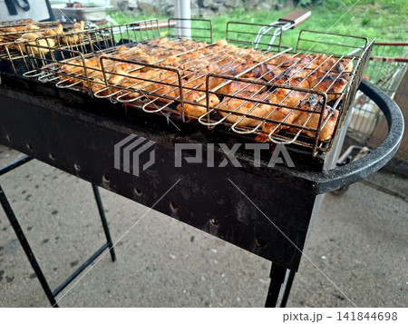 Golden juicy grilled chicken meat pieces cooking in wire mesh grate over outdoor barbecue charcoal mangal for summer picnic food preparation Golden juicy grilled chicken meat pieces cooking in wire mesh grate over outdoor barbecue charcoal mangal for summer picnic food preparation 141844698