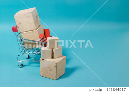 A small shopping cart filled with blank wooden blocks and stacked cubes on a vibrant blue background with copy space for text. High Quality Photo A small shopping cart filled with blank wooden blocks and stacked cubes on a vibrant blue background with copy space for text. High Quality Photo 141844917