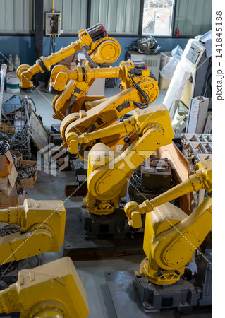 Vibrant yellow robotic arms stand in industrial workshop with visible cables and machinery Vibrant yellow robotic arms stand in industrial workshop with visible cables and machinery 141845188