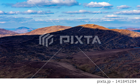 The wide-angle photograph displays a sequence of mountain chains receding into the distance under a bright sky. 141845284