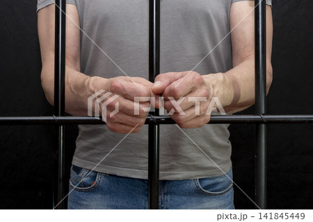Close-up of a prisoner's hands holding onto the bars. Close-up of a prisoner's hands holding onto the bars. 141845449
