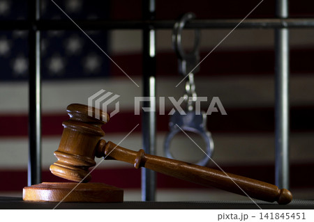 The judge's gavel against a background of the American flag, prison bars and handcuffs is a symbol of justice and the punishment system in the United States. 141845451
