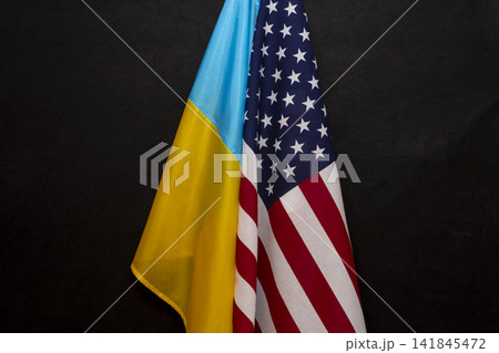 The flag of Ukraine and the flag of America are joined together on a black background, close-up, bends and waves on the flags. Concept: joint meeting, lend-lease assistance. 141845472