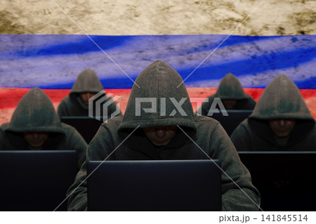 The troll factory. A hacker is sitting at a laptop and against the background of the Russian flag, attacking and hacking corporate servers with a virus. Concept: DDOS attack, fake news. The troll factory. A hacker is sitting at a laptop and against the background of the Russian flag, attacking and hacking corporate servers with a virus. Concept: DDOS attack, fake news. 141845514