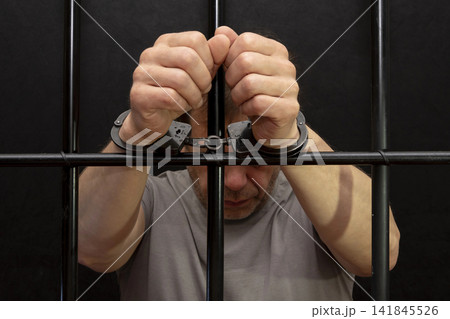 Arrested man handcuffed in jail holds on to the bars. Arrested man handcuffed in jail holds on to the bars. 141845526