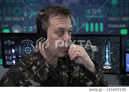 An elderly military man with headphones looks at the monitor. Concept: rocket launch, human observation, analytical center. An elderly military man with headphones looks at the monitor. Concept: rocket launch, human observation, analytical center. 141845530
