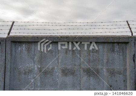 A concrete wall with barbed wire against an overcast sky is a symbol of restriction and security. 141846620