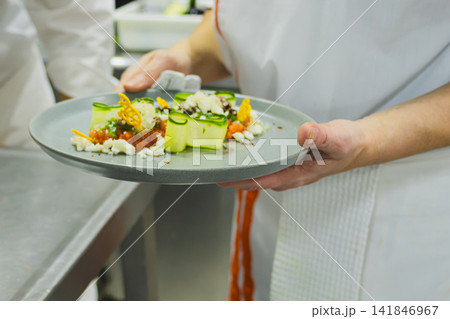 Professional chef presenting a creative and healthy gourmet dish, preparing exquisite international cuisine with innovation and sustainability for a unique gastronomic experience Professional chef presenting a creative and healthy gourmet dish, preparing exquisite international cuisine with innovation and sustainability for a unique gastronomic experience 141846967