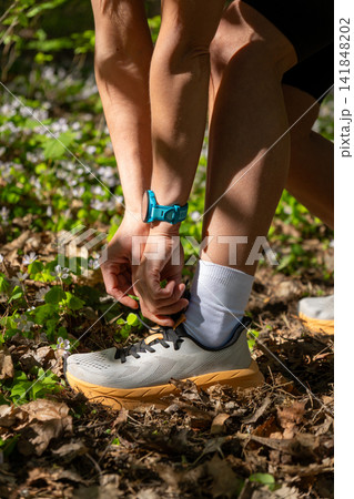 Close-up of a trail runner tying shoelace in a sunny spring forest Close-up of a trail runner tying shoelace in a sunny spring forest 141848202