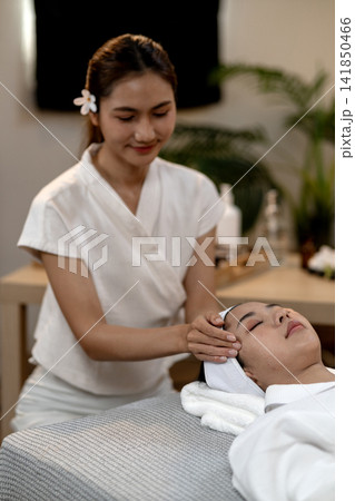 Asian woman spa therapist provides facial massage therapy to client enjoying relaxing skincare treatment professional beauty salon wellness center environment Asian woman spa therapist provides facial massage therapy to client enjoying relaxing skincare treatment professional beauty salon wellness center environment 141850466
