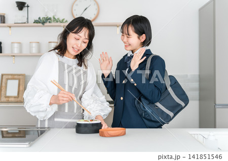 朝にキッチンで娘のお弁当を詰める母親と制服姿の女の子（お弁当作り） 141851546