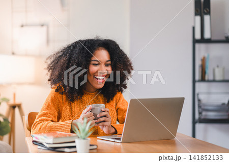 Smiling African American woman using a laptop while working from home. Smiling African American woman using a laptop while working from home. 141852133