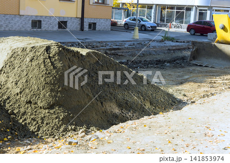 Construction work takes place on city street with dirt piles equipment Construction work takes place on city street with dirt piles equipment 141853974
