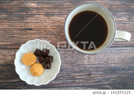 木製テーブルの上に置いたホットコーヒーとクッキーとチョコレート 木製テーブルの上に置いたホットコーヒーとクッキーとチョコレート 141855125