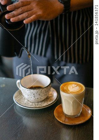 Barista pouring coffee with kettle and latte art in cafe with warm tones Barista pouring coffee with kettle and latte art in cafe with warm tones 141856371