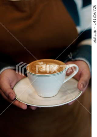 Latte art coffee served by person in white cup and saucer Latte art coffee served by person in white cup and saucer 141856726
