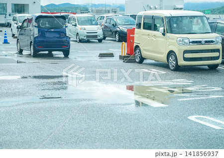 雨に濡れた駐車場に並ぶ車と水たまりの反射 雨に濡れた駐車場に並ぶ車と水たまりの反射 141856937