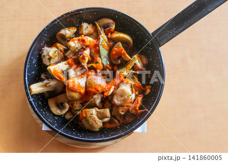 Sliced mushrooms and octopus with garlic and sauce in a hot cast-iron skillet on a table Sliced mushrooms and octopus with garlic and sauce in a hot cast-iron skillet on a table 141860005