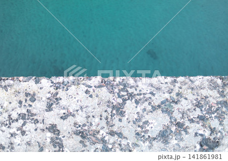 Top view of turquoise water beside a rough weathered concrete edge, creating an abstract geometric composition with contrasting textures, minimal design and refreshing aquatic tones Top view of turquoise water beside a rough weathered concrete edge, creating an abstract geometric composition with contrasting textures, minimal design and refreshing aquatic tones 141861981