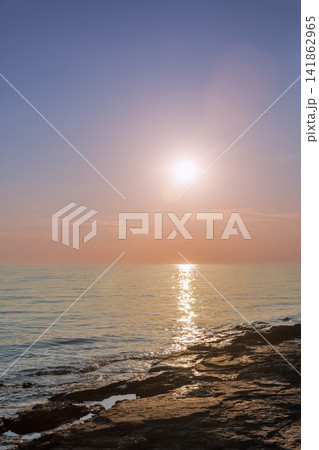 Sunset over calm sea and rocky shore. 141862965
