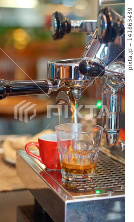 Fresh espresso flowing from a portafilter into a glass on an espresso machine, showing coffee extraction, professional brewing technique, cafe service, and specialty coffee. 141863439