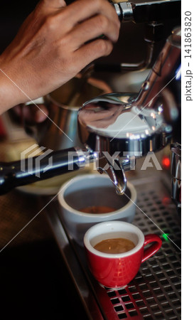 Barista preparing specialty espresso with portafilter and red espresso cup in a warm cafe atmosphere Barista preparing specialty espresso with portafilter and red espresso cup in a warm cafe atmosphere 141863820