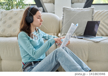 Focused teen student girl in headphones reading book sitting floor Focused teen student girl in headphones reading book sitting floor 141863946
