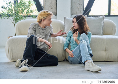 Young student friends sitting on living room floor having conversation Young student friends sitting on living room floor having conversation 141863960
