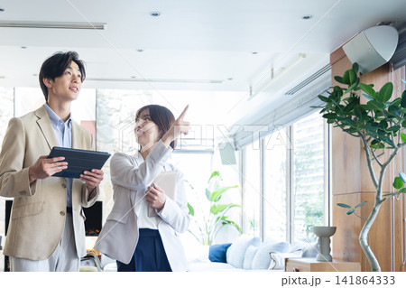 タブレットを手にオフィス内を指差して案内する女性と話を聞く男性ビジネスパーソン タブレットを手にオフィス内を指差して案内する女性と話を聞く男性ビジネスパーソン 141864333