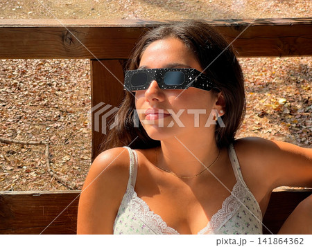 Woman Wearing Eclipse Glasses Outdoors on a Sunny Day Woman Wearing Eclipse Glasses Outdoors on a Sunny Day 141864362