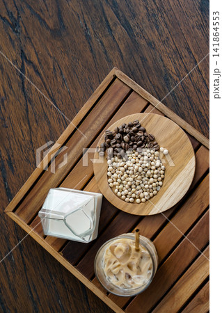 Flat Lay of Coffee Beans, Soybeans, Soy Milk, and Iced Latte on Wooden Tray for Plant Based Beverage and Cafe Lifestyle Concept Flat Lay of Coffee Beans, Soybeans, Soy Milk, and Iced Latte on Wooden Tray for Plant Based Beverage and Cafe Lifestyle Concept 141864553