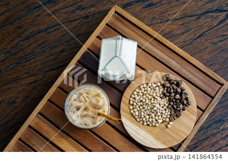 Flat Lay of Coffee Beans, Soybeans, Soy Milk, and Iced Latte on Wooden Tray for Plant Based Beverage and Cafe Lifestyle Concept 141864554