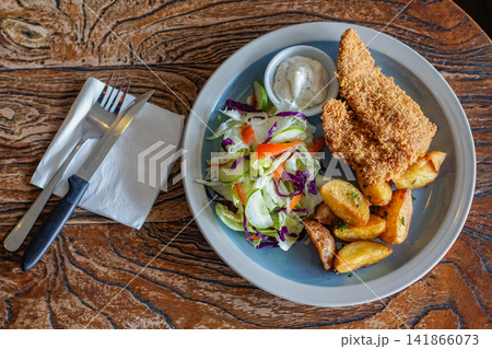A crispy fried chicken meal with potatoes, salad, and sauce, photographed from above on a rustic table A crispy fried chicken meal with potatoes, salad, and sauce, photographed from above on a rustic table 141866073