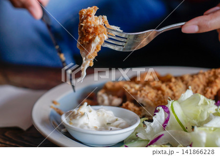 Close-up of a fork lifting a crispy breaded bite with dipping sauce and fresh salad 141866228