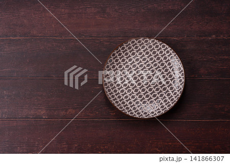 An empty round ceramic plate on a dark, textured brown background. An empty round plate An empty round ceramic plate on a dark, textured brown background. An empty round plate 141866307
