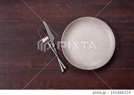 An empty round ceramic plate on a dark, textured brown background. An empty round plate An empty round ceramic plate on a dark, textured brown background. An empty round plate 141866314