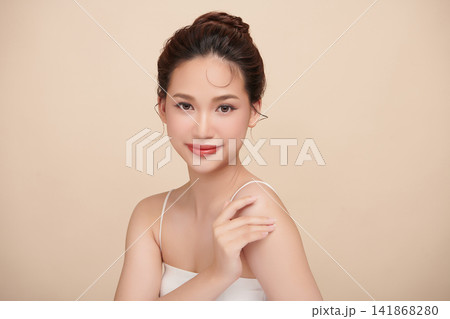 A beautiful young Asian woman with clean, fresh skin against a beige background. Skincare, facial treatment, cosmetology, beauty, and spa. An elegant portrait of an Asian woman. 141868280