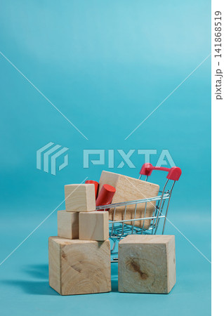 Creative composition of wooden cubes stacked around a mini shopping cart on a blue backdrop. High Quality Photo 141868519