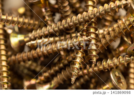 A close-up of a pile of shiny gold-colored wood screws with heads scattered randomly as a background 141869098