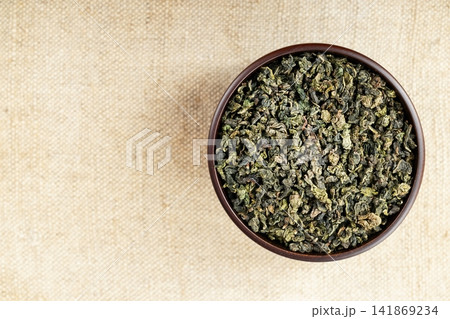 Rustic wooden bowl filled with Tie Guan Yin on beige burlap texture Rustic wooden bowl filled with Tie Guan Yin on beige burlap texture 141869234