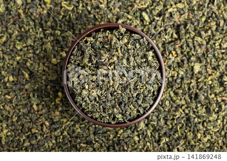 Wooden cup full of green oolong surrounded by loose tea texture 141869248