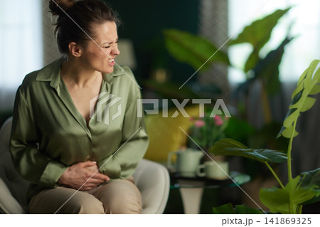 Woman Grimacing with Stomach Pain in Cozy Home Woman Grimacing with Stomach Pain in Cozy Home 141869325