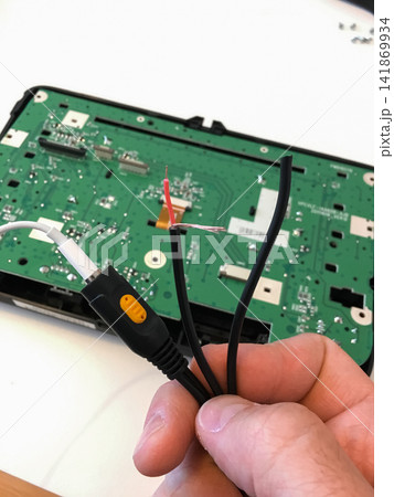 Hand holding a black connector and cables near the green circuit board of a car radio. Hand holding a black connector and cables near the green circuit board of a car radio. 141869934
