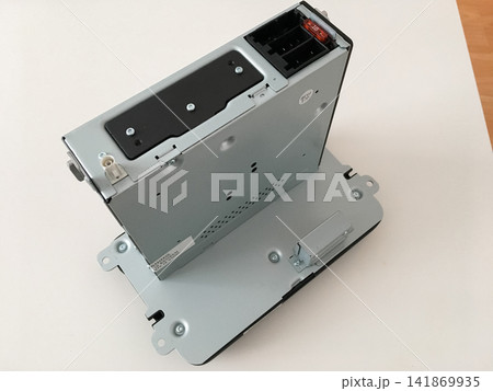 Car radio unit standing on a white table showing its metal mounting bracket and casing. 141869935