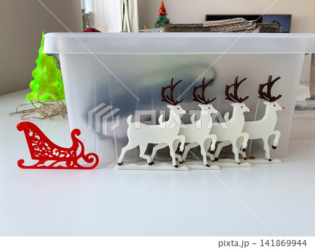 A collection of white reindeer figurines and a red sleigh ornament stand on a desk for Christmas holiday preparation A collection of white reindeer figurines and a red sleigh ornament stand on a desk for Christmas holiday preparation 141869944