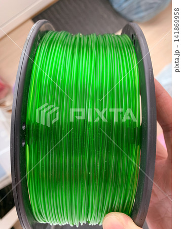 Close-up shot of a translucent green 3D printing filament spool held in a hand for inspection of quality Close-up shot of a translucent green 3D printing filament spool held in a hand for inspection of quality 141869958