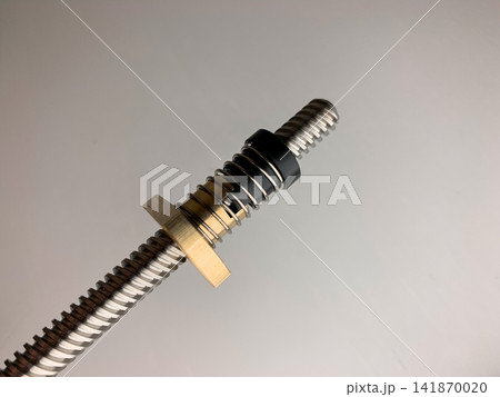 A close up of a metallic threaded lead screw with a brass nut component on a plain white surface A close up of a metallic threaded lead screw with a brass nut component on a plain white surface 141870020