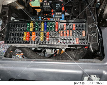 A detailed view of a car fuse box with colorful electrical fuses inserted in a black plastic holder under the dashboard A detailed view of a car fuse box with colorful electrical fuses inserted in a black plastic holder under the dashboard 141870278